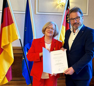 Eine Frau und ein Mann mit Urkunde vor Flaggen