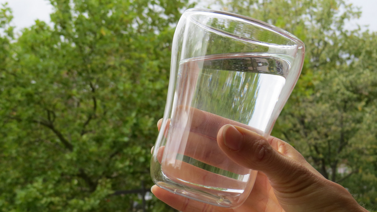 gefülltes Wasserglas vor Bäumen