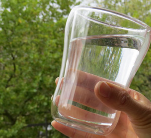 gefülltes Wasserglas vor Bäumen