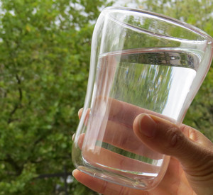 gefülltes Wasserglas vor Bäumen
