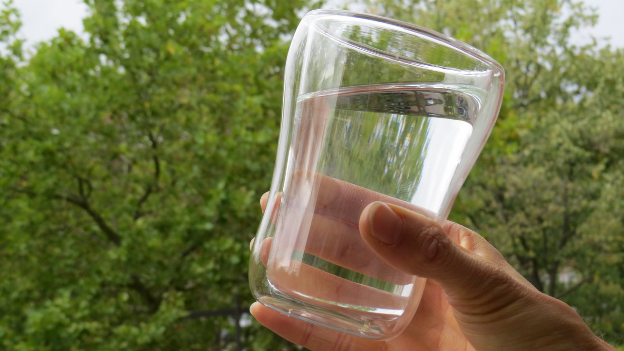 gefülltes Wasserglas vor Bäumen