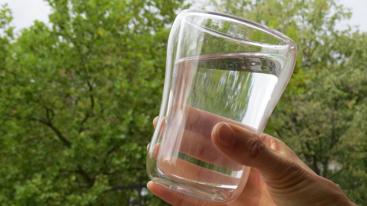 gefülltes Wasserglas vor Bäumen