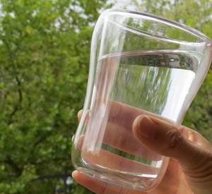 gefülltes Wasserglas vor Bäumen