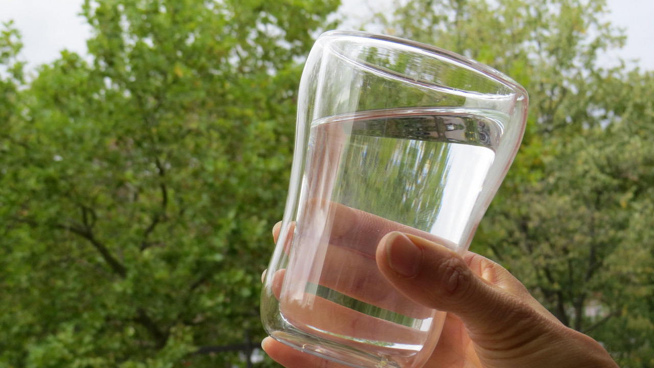 gefülltes Wasserglas vor Bäumen