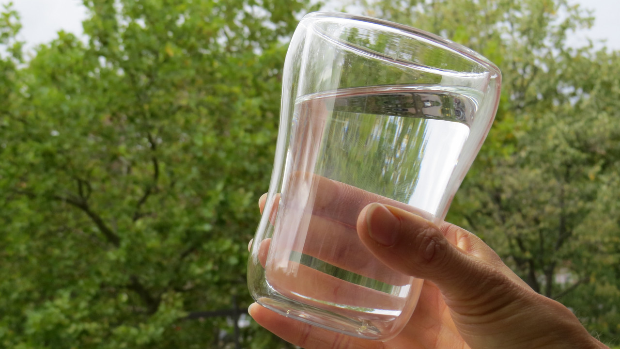 gefülltes Wasserglas vor Bäumen