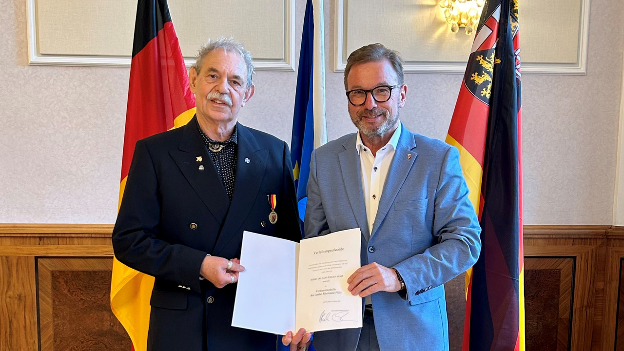 Zwei Männer vor Flaggen mit Urkunde