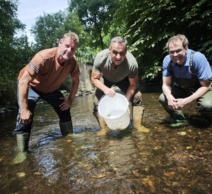 Drei Männer mit Gummistiefeln und Eimer hocken im flachen Wasser 