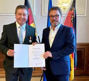 Zwei Männer mit Urkunde vor Flaggen