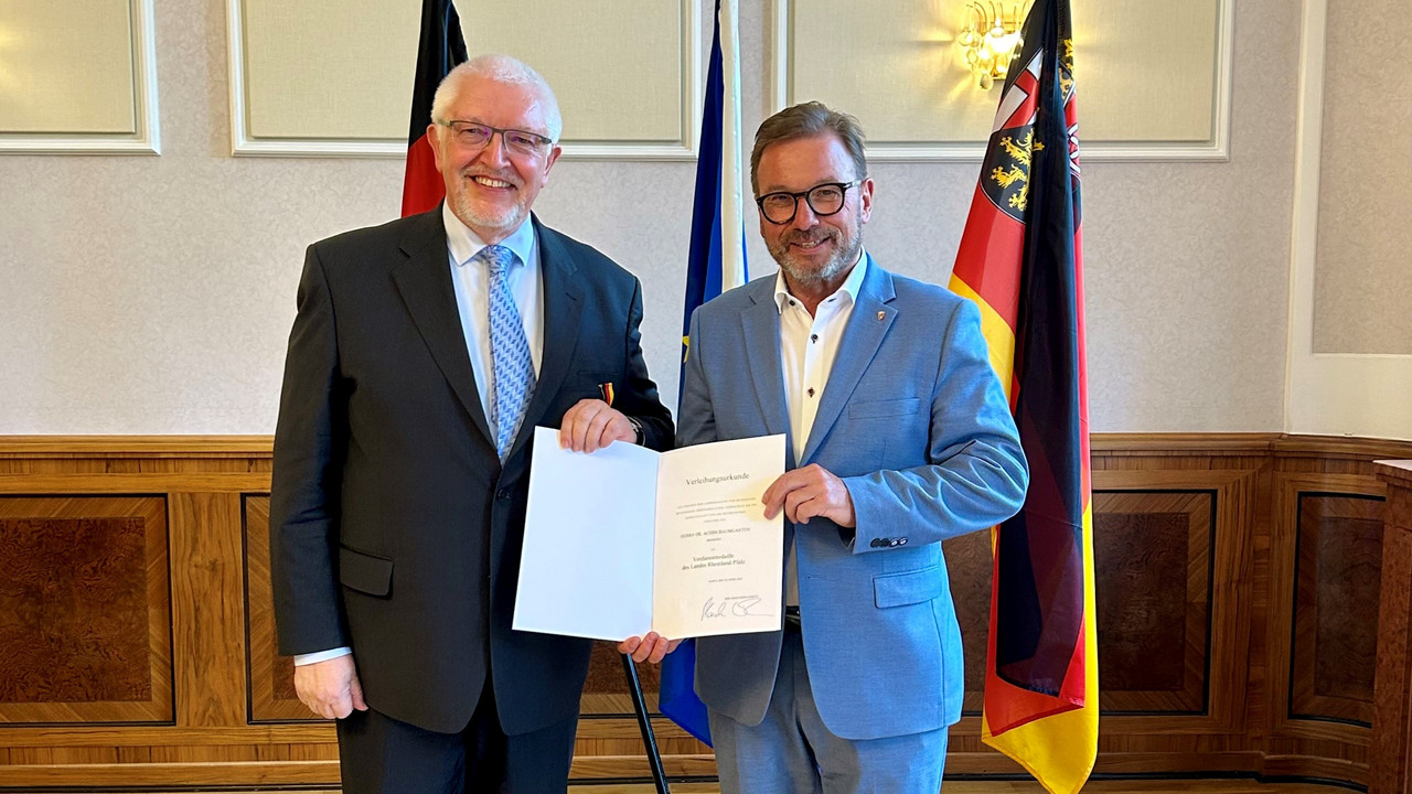 Zwei Männer vor Flaggen mit Urkunde