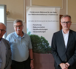 Drei männliche Personen vor einem Plakat